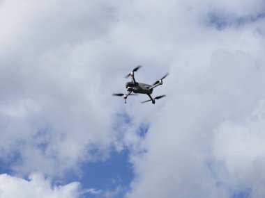 Mavi gökyüzünde bulutlarla uçan bir dron.