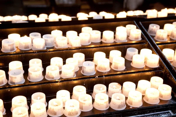 Primo piano di candele che bruciano in una chiesa su tre ripiani — Foto Stock