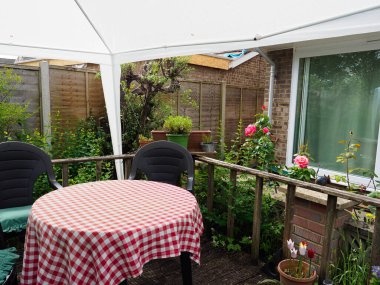 Arka bahçedeki küçük bir süsleme alanı beyaz bir çardakla kaplı ve bir masa gösteriyor.