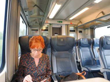 Yetişkin bir kadın, trende görünürde başka kimse yokken cep telefonunu kontrol ediyor.