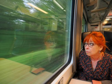 Yetişkin bir bayan, trende başka kimse yokken gergin bir şekilde pencereden dışarı bakıyor.