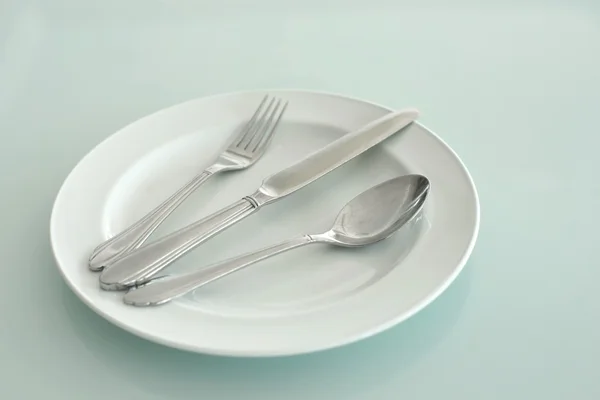 Spoon fork and knife on empty white plate — Stock Photo, Image