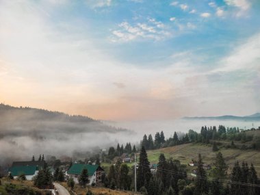 Yazın gün batımında yağan yağmurdan sonra kırsal ahşap evlerle rüya gibi dağların üzerinde beyaz sis..