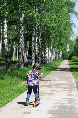 Parkta scooter süren bir çocuğun yakın çekimi. Küçük bir çocuk scooter sürmeyi öğreniyor. Güneşli yaz günü