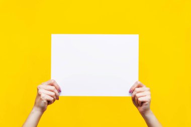 Tasarım için şablon. Parlak sarı arka planda izole edilmiş kadın ellerinde metin ya da tasarım için boş bir kopya alanı olan beyaz sayfa. Reklamlar, reklamlar, mitingler, toplantılar, protestolar için boş maket