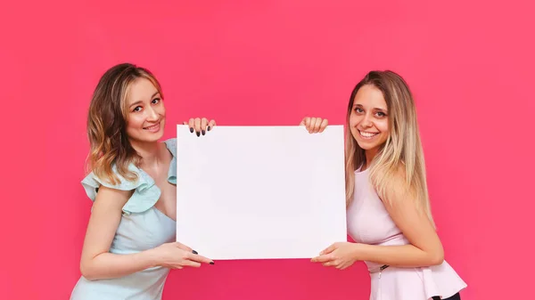 2人の若い白人女性プロモーターは 明るい色のピンクの背景にテキストやデザインのための空のコピースペースを持つホワイトボードを保持しています プロモーション用のテンプレート 広告のためのモックアップブランク — ストック写真