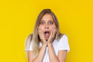 Beyaz tişörtlü, beyaz saçlı, genç, güzel, beyaz, sarışın bir kadın satış haberleri karşısında şaşırdı ve indirimler sarı arka planda izole edildi. 