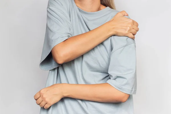 灰色の背景に隔離された彼女の手の肩を持つ灰色のTシャツの若い女性の作物のショット 肩の怪我 腕の痛み 神経痛 — ストック写真