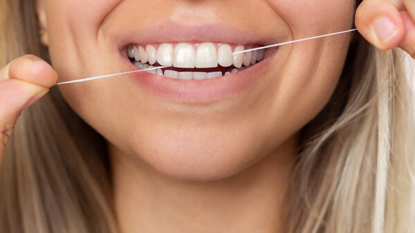 Close-up of female teeth. A Young beautiful woman cleans her teeth with dental floss. Dental concept