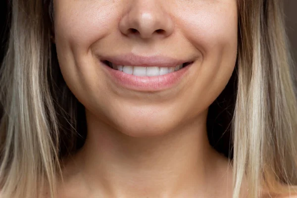 Cropped shot of a face of a young caucasian smiling blonde woman with dimples on her cheeks. Close up