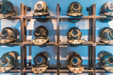 Bir grup eski metal dalış kaskı, odada tozlanmış.