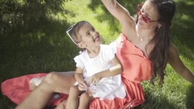 Küçük güzel bir kız ve annesi çimenlerin üzerinde oyuncaklarla oynuyorlar.