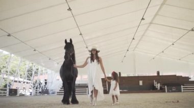 Annesiyle yarış pistinde güzel siyah bir atı olan küçük güzel bir kız.