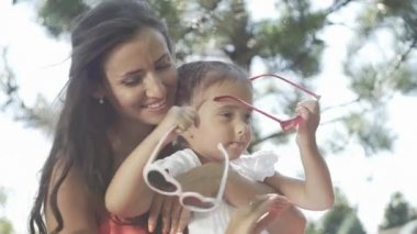 Küçük güzel bir kız ve annesi çimenlerin üzerinde oyuncaklarla oynuyorlar.