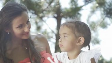 Küçük güzel bir kız ve annesi çimenlerin üzerinde oyuncaklarla oynuyorlar.