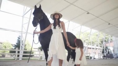 Annesiyle yarış pistinde güzel siyah bir atı olan küçük güzel bir kız.