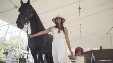 Annesiyle yarış pistinde güzel siyah bir atı olan küçük güzel bir kız.