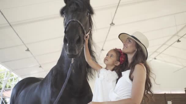 小さな美しいです女の子とともにお母さんオン競馬場とともに黒美しい馬 — ストック動画