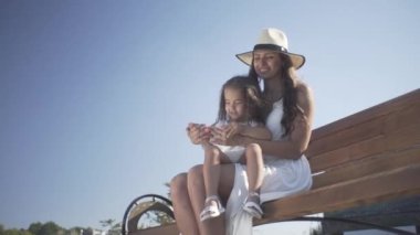 Annesiyle küçük güzel bir kız bankta oturur ve parkta yürür.