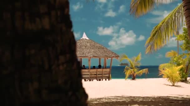 Pabellón de madera en la playa de arena blanca bajo palmeras con algunas personas — Vídeo de stock