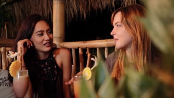 Caucásico y asiático mujeres charlando en un bar con bebidas, riendo — Vídeos de Stock