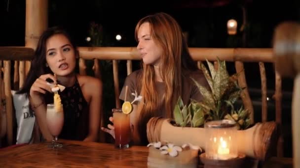 Caucásico y asiático mujeres charlando en un bar con bebidas, sonriendo — Vídeos de Stock