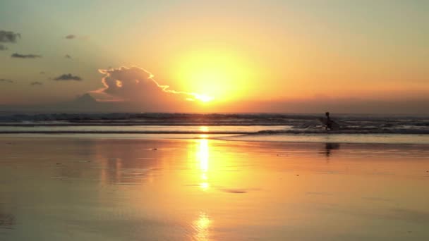 Plage au coucher du soleil, garçon avec planche de surf traversant les vagues — Video