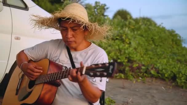 Indonesische man gitaar spelen en zingen op strand — Stockvideo