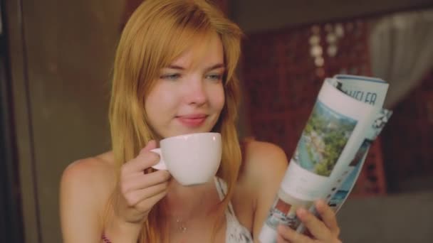 Young woman drinking coffee in rustic cafe, reading magazine — Stock Video