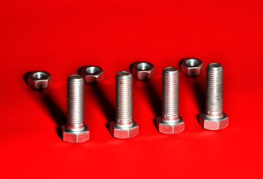 Kırmızı arka planda gölgeli metal cıvatalar ve fındıklar. Donanım