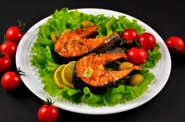 Beyaz tabakta pişmiş alabalık. Siyah arkaplan.