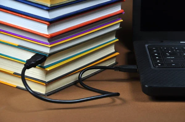 E-learning education internet library. A laptop and a stack of books connected by a cable.