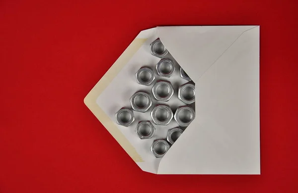 オンライン配信 赤い背景に郵便封筒と金属ナッツ — ストック写真
