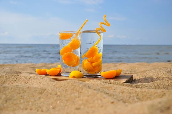 Peach cold drink with a straw on a sandy beach.