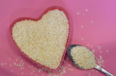 Pembe arka planda kalp şeklinde beyaz susam tohumları, üst manzara. Süper yemek malzemesi. Sağlıklı vegan kavramı