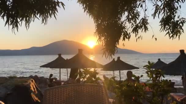 Sonnenuntergang am Meer mit Silhouetten von Menschen und Sonnenschirmen — Stockvideo