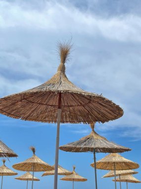 Mavi gökyüzü ve deniz arka planında saman plaj şemsiyeleri. Boşluğu kopyala 