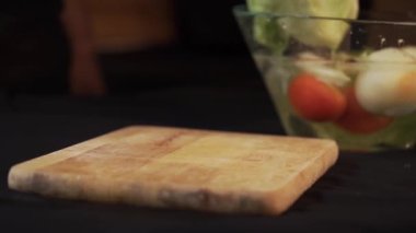 Ahşap kesim tahtasına salata koyup kesen bir erkek şef. Siyah arkaplan