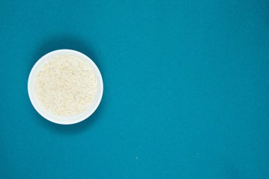 Beyaz seramik kasede uzun tahıllı beyaz pirinç, arka planda bir renk. Boşluğu kopyala