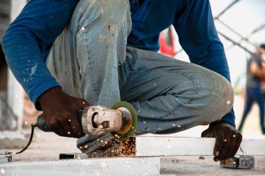 Yan taraflarda, değirmen makinesinden parlak kıvılcımlar uçuşuyor. Genç bir kaynakçı garajda metal bir ürün öğütüyor.