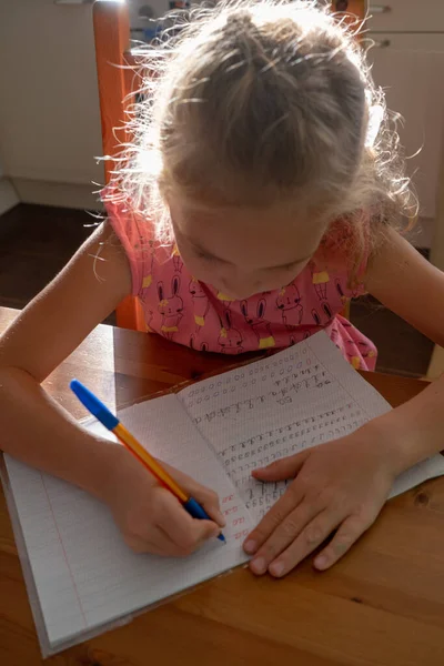 La ragazzina di prima elementare scrive lettere in un quaderno. — Foto Stock