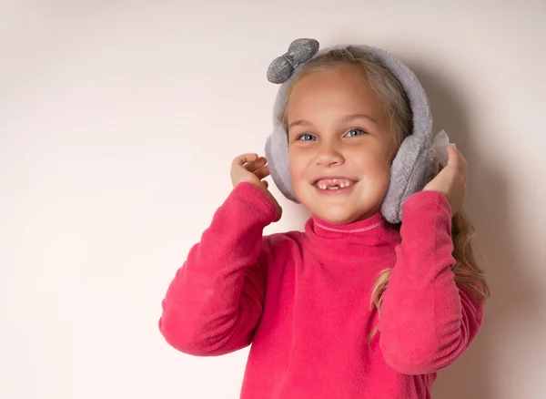 Pequeña linda chica sin dientes tonteando con auriculares de piel caliente sobre un fondo claro. —  Fotos de Stock