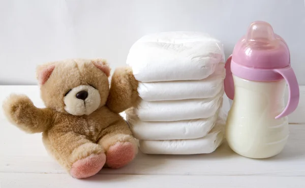 New born child stack of diapers, tebby bear toy and baby feeding bottle — Stock Photo, Image