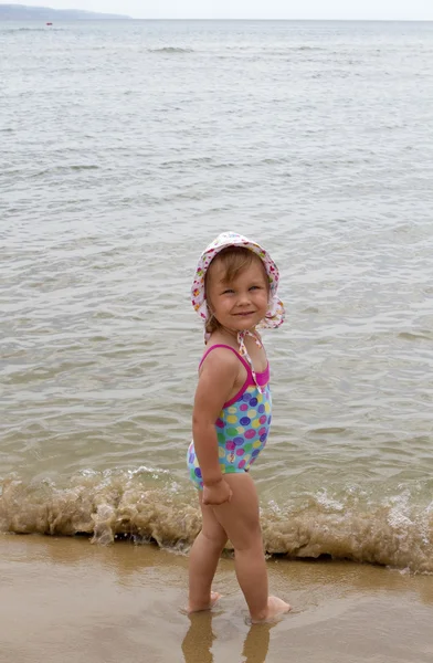 Klein meisje in een badpak tegen de zee is het zand — Stockfoto