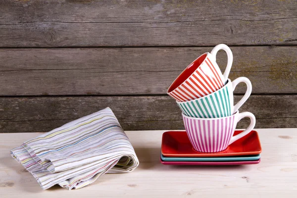 Copos de café listrados coloridos na prateleira e toalha de algodão — Fotografia de Stock