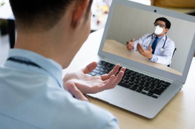 Genç iş adamının ofisinde bileği ağrıyormuş. Bu yüzden Asyalı doktora danışmak için video konferansına gitmiş. teletıp konsepti (eldeki odaklanma)