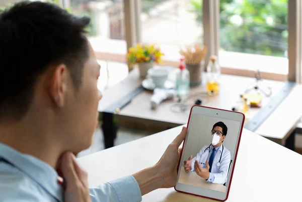 young businessman has sore throat from cold at office, so he consult asian doctor online via video call conference to ask for advice. telemedicine concept