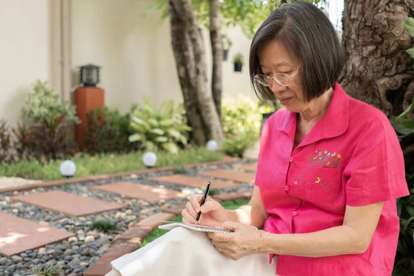 senior retired woman writing diary and sitting in backyard at home