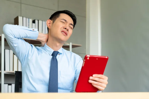 年轻的亚洲商人在与计算机长期合作后感到脖子疼痛 他使用平板电脑在网上看医生 办公室综合症概念 — 图库照片