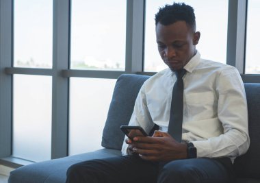 portrait of young african businessman with smiling face, using smartphone in office. business concept